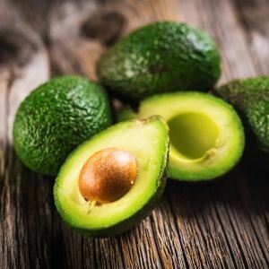 A whole avocado with one half sliced open in front of it, showing the brown stone and light green flesh